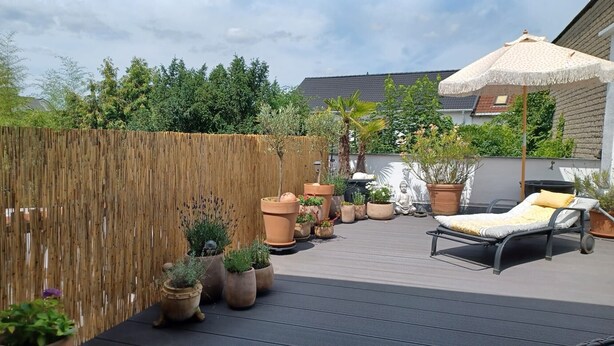 A rooftop patio with a wooden fence, potted plants, a reclining chair, and a large umbrella.