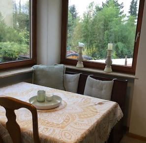 Un comedor con una mesa dispuesta para dos, una ventana que da a vistas de árboles y un radiador debajo de la ventana.