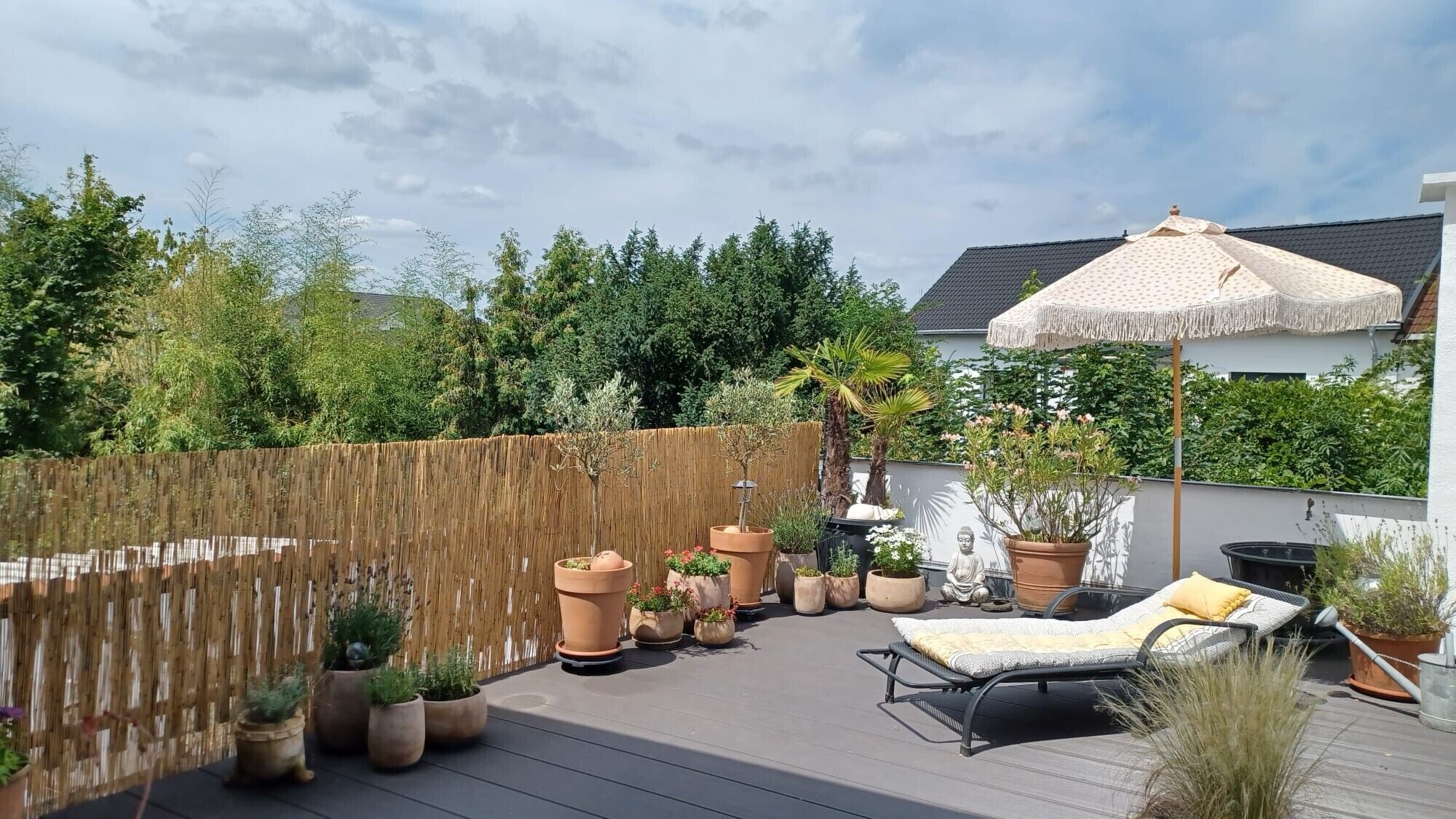 Eine Dachterrasse mit Holzdeck, Topfpflanzen, einem Liegestuhl und einem großen Sonnenschirm.