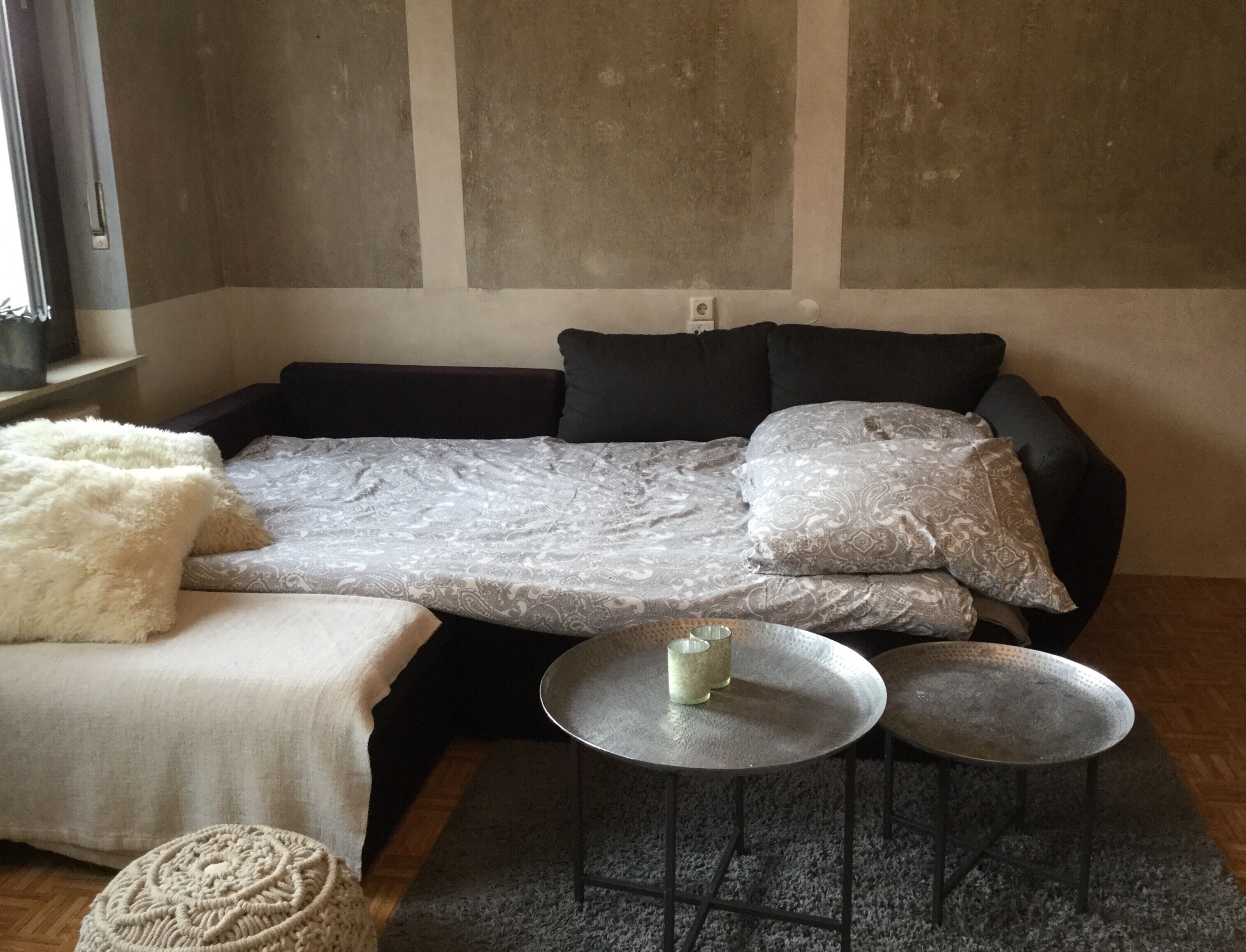 Un soggiorno moderno con un divano, due tavolini rotondi, una soffice coperta bianca e un pouf in macramè.
