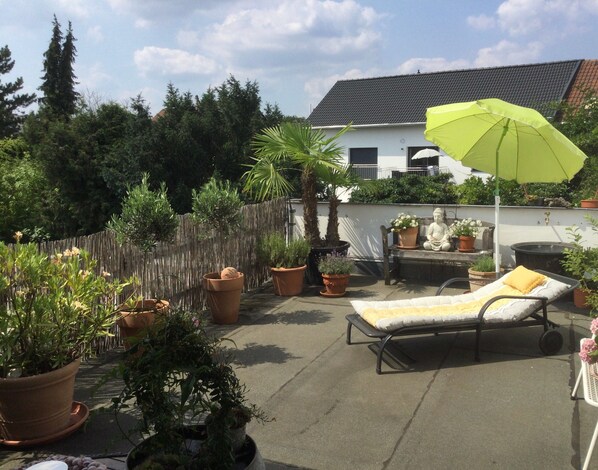 A patio with a lounge chair, a bench, potted plants, a statue, and a green umbrella. - Beletage Holiday Apartment with Large South-Facing Terrace in Neuwied (Neuwied)