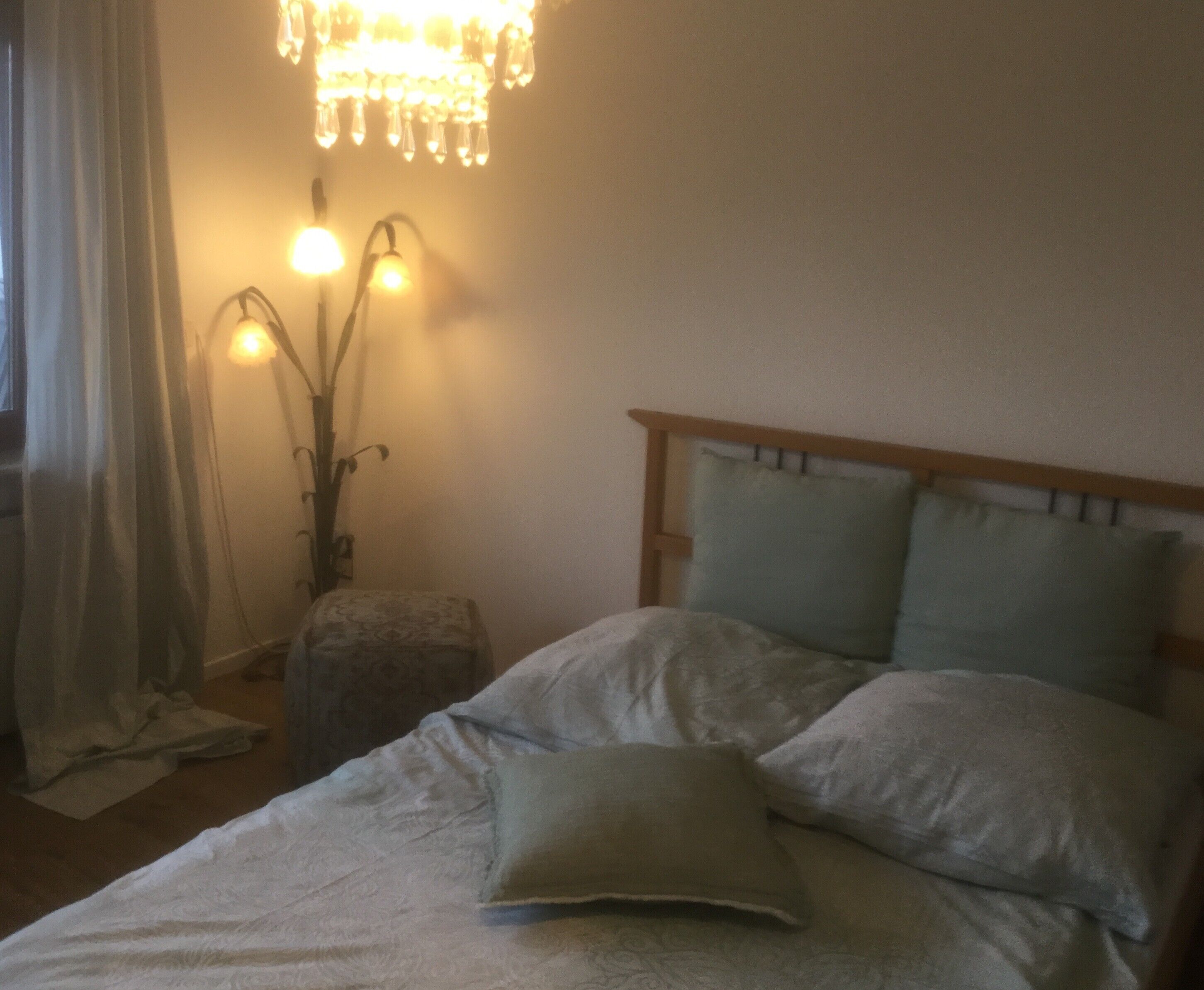 Une chambre à coucher avec un lit, des oreillers, une table de chevet, une lampe et une fenêtre avec des rideaux.