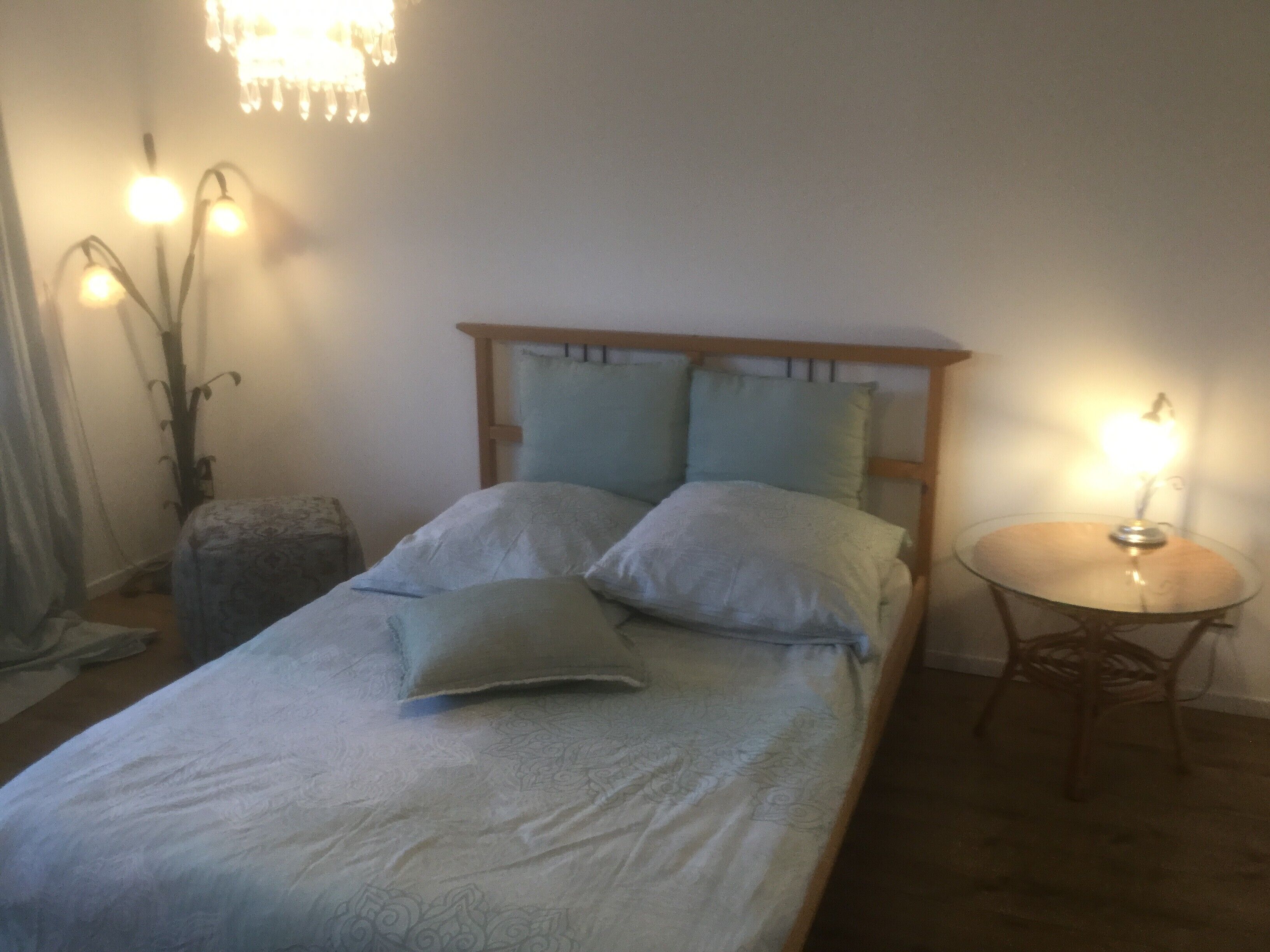 Un lit simple avec une tête de lit en bois, deux oreillers, une table de chevet avec une lampe et une lampe sur pied avec plusieurs ampoules.