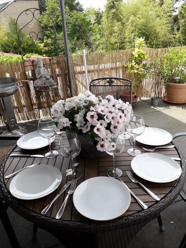 Un espacio al aire libre para comer con mesas de mimbre, platos blancos y copas de vino para cuatro personas.
