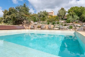 En swimmingpool med klart, blåt vand, omgivet af sten og træer, samt en bygning i baggrunden.
