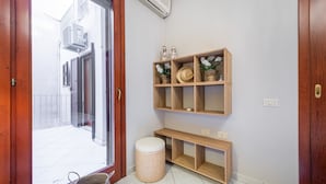 A room with a sliding glass door leading to a balcony, a wooden shelf with decorative items, a woven stool, and a small wooden table. - Apartment "Suite Home Simius" Close to Beach with Terrace, Sea View & Air Conditioning (Villasimius)