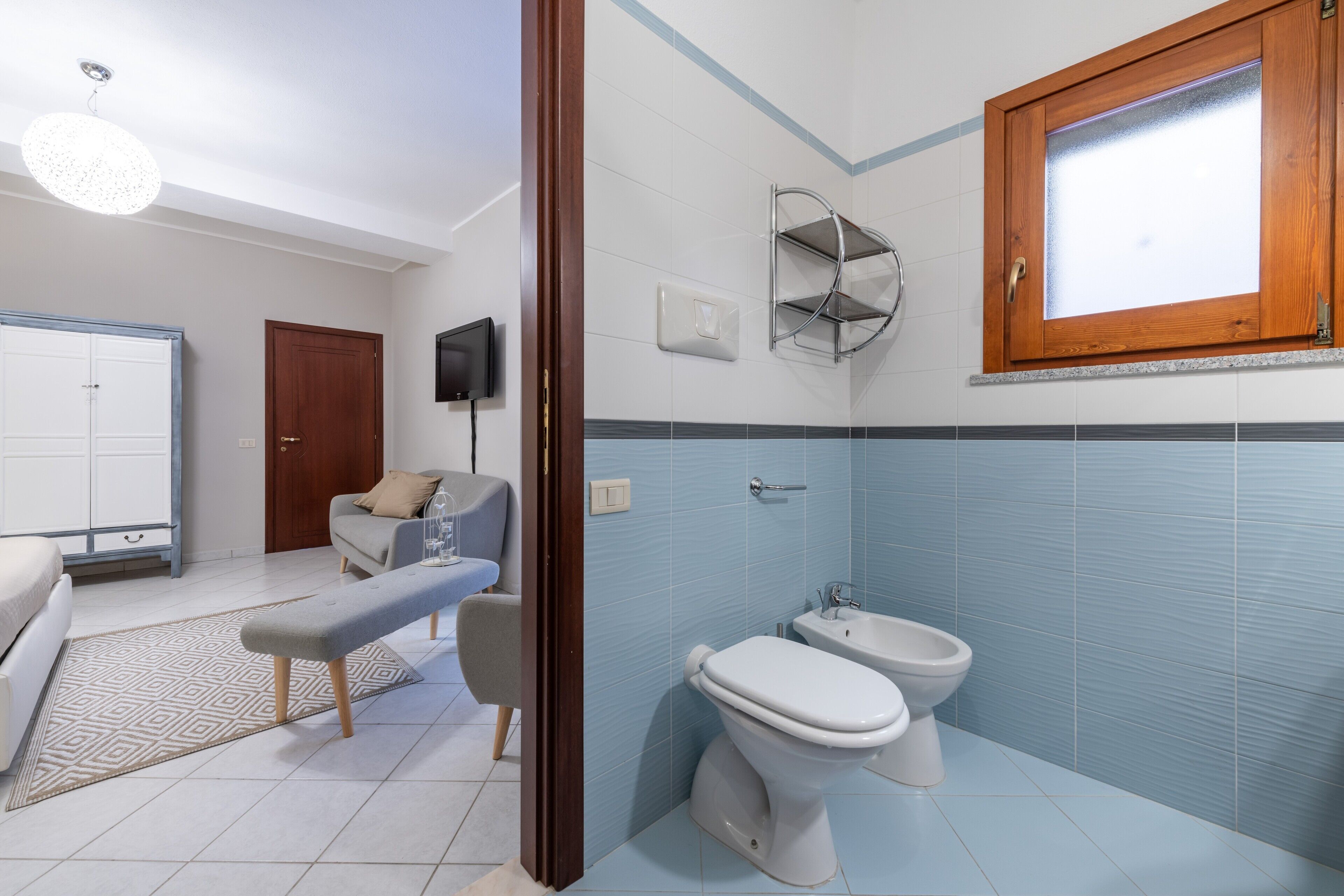 A bathroom with a toilet, bidet, and a wooden-framed window.