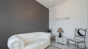 A white leather sofa, a patterned rug, a lamp, a chair, and a star-shaped wall decoration in a room with a grey wall and white floor tiles. - Apartment "Suite Home Simius" Close to Beach with Terrace, Sea View & Air Conditioning (Villasimius)