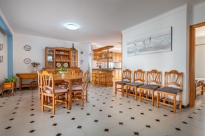 A dining area with a wooden table and chairs, a kitchen with wooden cabinets, and a painting on the wall.