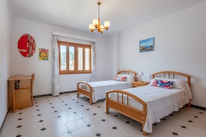 A room with two wooden beds, a desk, a chair, a window with curtains, a chandelier, and a painting on the wall.