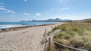 Una playa con una cerca de madera, orilla arenosa y montañas a lo lejos.