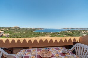 A balcony with a table and chairs, overlooking a coastal landscape with greenery and a body of water. - Holiday Apartment with Sea View and Terrace Steps from Palau Center (Palau)