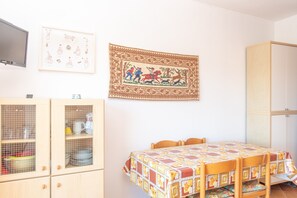 Une pièce comprenant une table en bois, des chaises, un meuble avec des portes en verre et une tapisserie encadrée accrochée au mur.