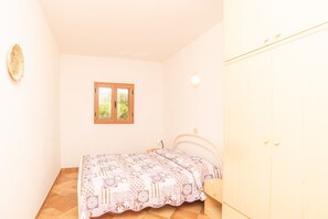 Une chambre à coucher comprenant un lit, une armoire, une fenêtre et un luminaire fixé au mur.