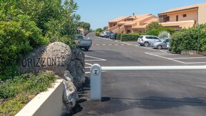Un espace de stationnement clos, avec un panneau en pierre portant l’inscription « ORIZZONTE », une entrée fermée par un portail et des véhicules stationnés.