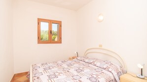 Une chambre à coucher comprenant un lit, une table de chevet, une lampe, une fenêtre et un luminaire fixé au mur.