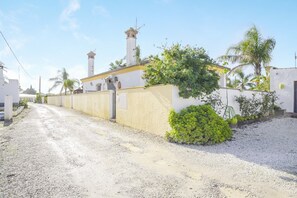 Rua residencial com um prédio branco, entrada de automóveis em cascalho e um pequeno jardim.