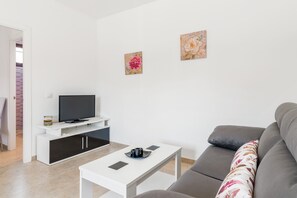 Una sala de estar moderna con un televisor de pantalla plana, una mesa de centro blanca, un sofá gris y dos piezas de arte floral en las paredes.