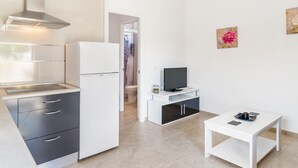 Een compacte keuken met een koelkast, fornuis en een klein tafeltje met een flatscreen-tv.
