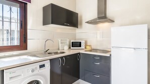 Een compacte keuken met een wasmachine, een magnetron, een koelkast en een raam met uitzicht.