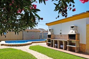 Un patio trasero con piscina, parrillas de barbacoa y un patio de baldosas.