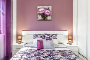 Un dormitorio con cama, dos mesitas de noche, un cuadro en la pared y una ventana.