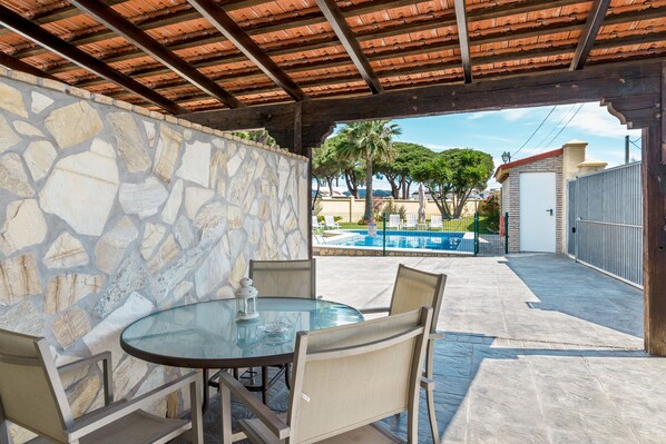 Un patio cubierto con un muro de piedra, una mesa de vidrio y sillas de mimbre.