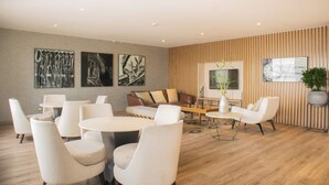 A modern lounge area with a sofa, chairs, and a coffee table. There are wall art pieces and a potted plant.
