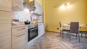 A modern kitchen with wooden cabinets, a built-in oven, and a dining area with a checkered tablecloth. - Spacious Holiday Home “Paradise Home” with Wi-Fi & Balcony (Quartu Sant'Elena)