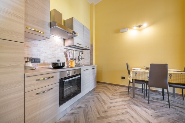 A modern kitchen with wooden cabinets, a built-in oven, and a dining area with a checkered tablecloth.