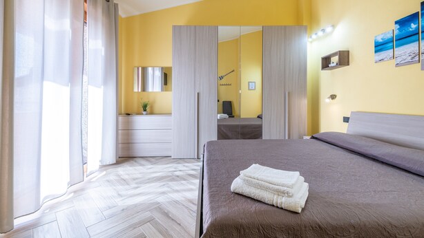 A hotel room with a bed, a mirror, a bedside table, a wardrobe, and a bathroom visible through a door. - Spacious Holiday Home “Paradise Home” with Wi-Fi & Balcony (Quartu Sant'Elena)