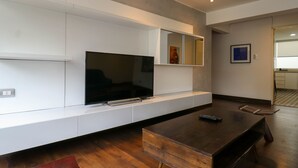 A modern living room with a flat-screen TV mounted on a white wall, a wooden coffee table, and a remote control on it. - w* | Luxury 2BR in Blas Cerdeña, San Isidro (Cercado de Lima)