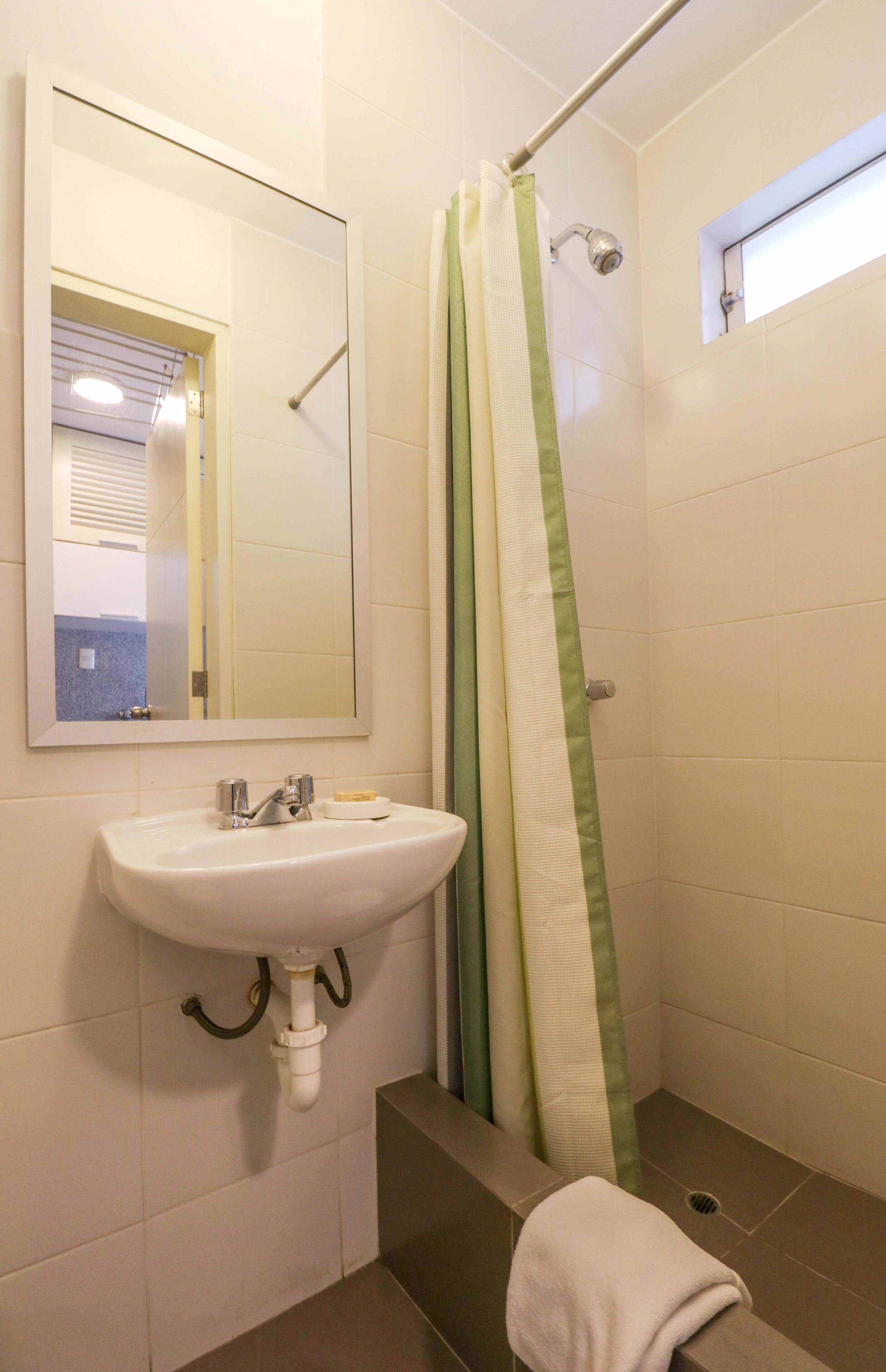 Un bagno con un lavandino bianco, uno specchio e una doccia con tenda verde.