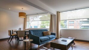 A modern living room with a blue sofa, a wooden coffee table, and a dining area with chairs and a small table. - w* | Luxury 2BR in Blas Cerdeña, San Isidro (Cercado de Lima)