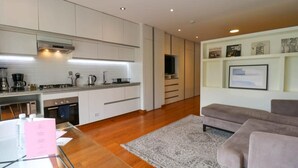 A modern kitchen with white cabinets, a built-in oven, and a coffee machine. There is a grey sofa and a rug in the living area. - w* | Elegant Loft Near Boardwalk in Barranco (Barranco)