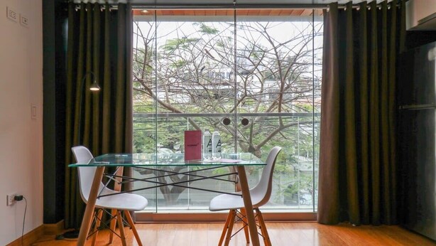 A dining area with a glass table and white chairs, a red bag, and a view of trees through a large window. - w* | Elegant Loft Near Boardwalk in Barranco (Barranco)