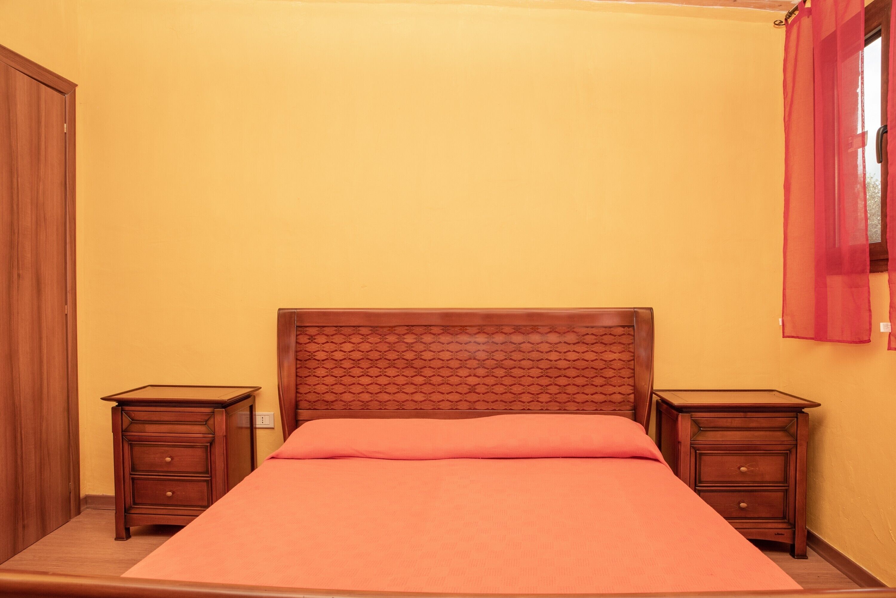 A bedroom with a wooden headboard, a single bed with a pink bedspread, two wooden nightstands, and a wooden door.