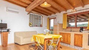 A cozy room with a wooden ceiling, a sofa, a dining table with yellow chairs, a kitchen area, and a window with curtains. - Résidence Villa Smeralda Executive – Upscale Apartment with Pool near Olbia (Telti)