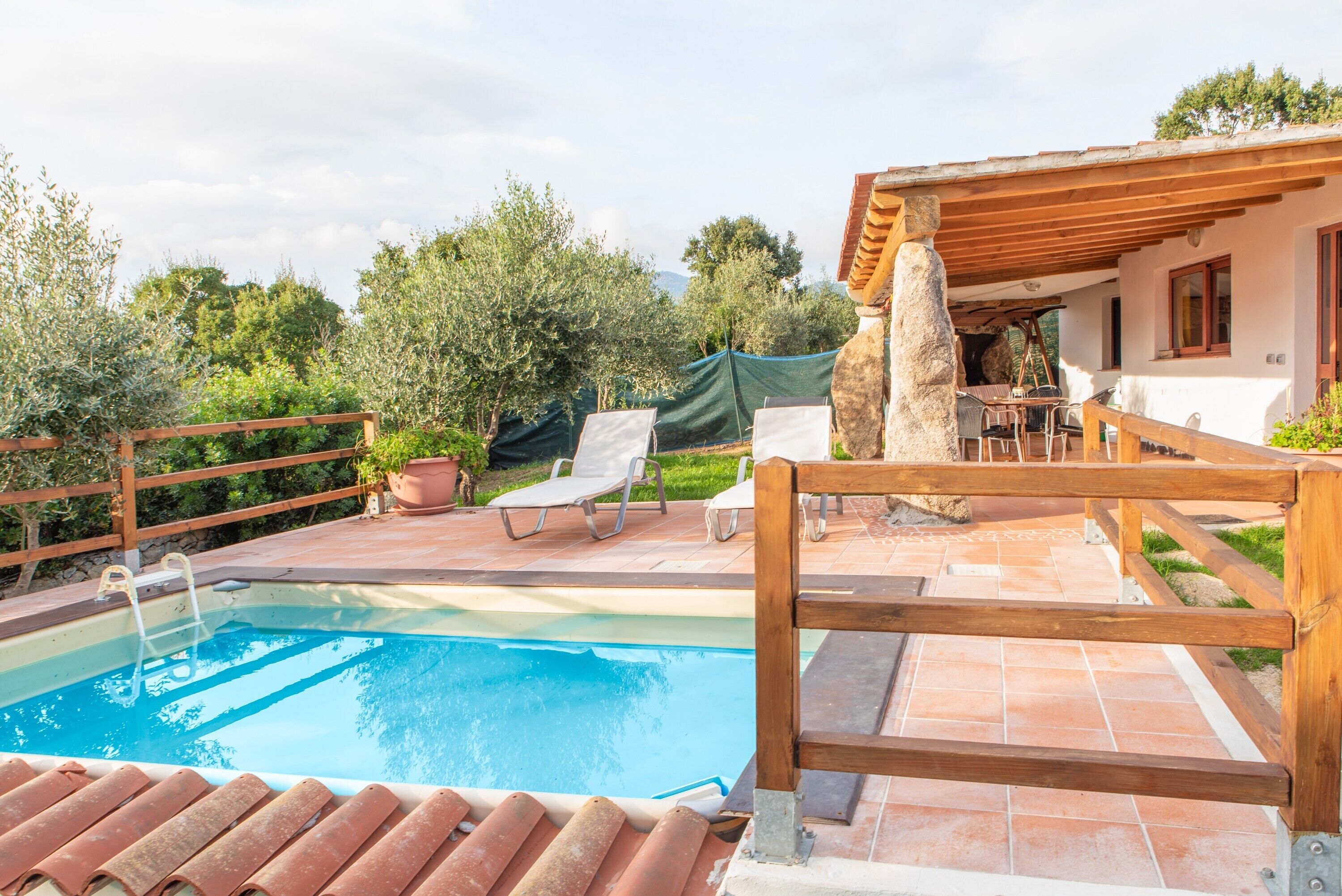 A swimming pool with a wooden deck, lounge chairs, and a stone pillar.