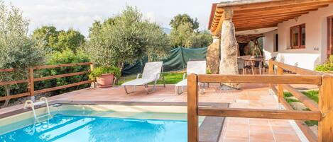 A swimming pool with a wooden deck, lounge chairs, and a stone pillar.