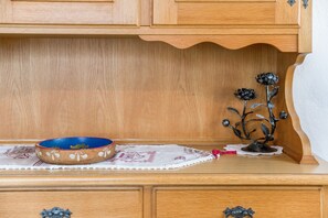 Un meuble en bois orné d’une branche décorative en métal et surmonté d’un bol bleu posé sur un dessous de plat en dentelle.
