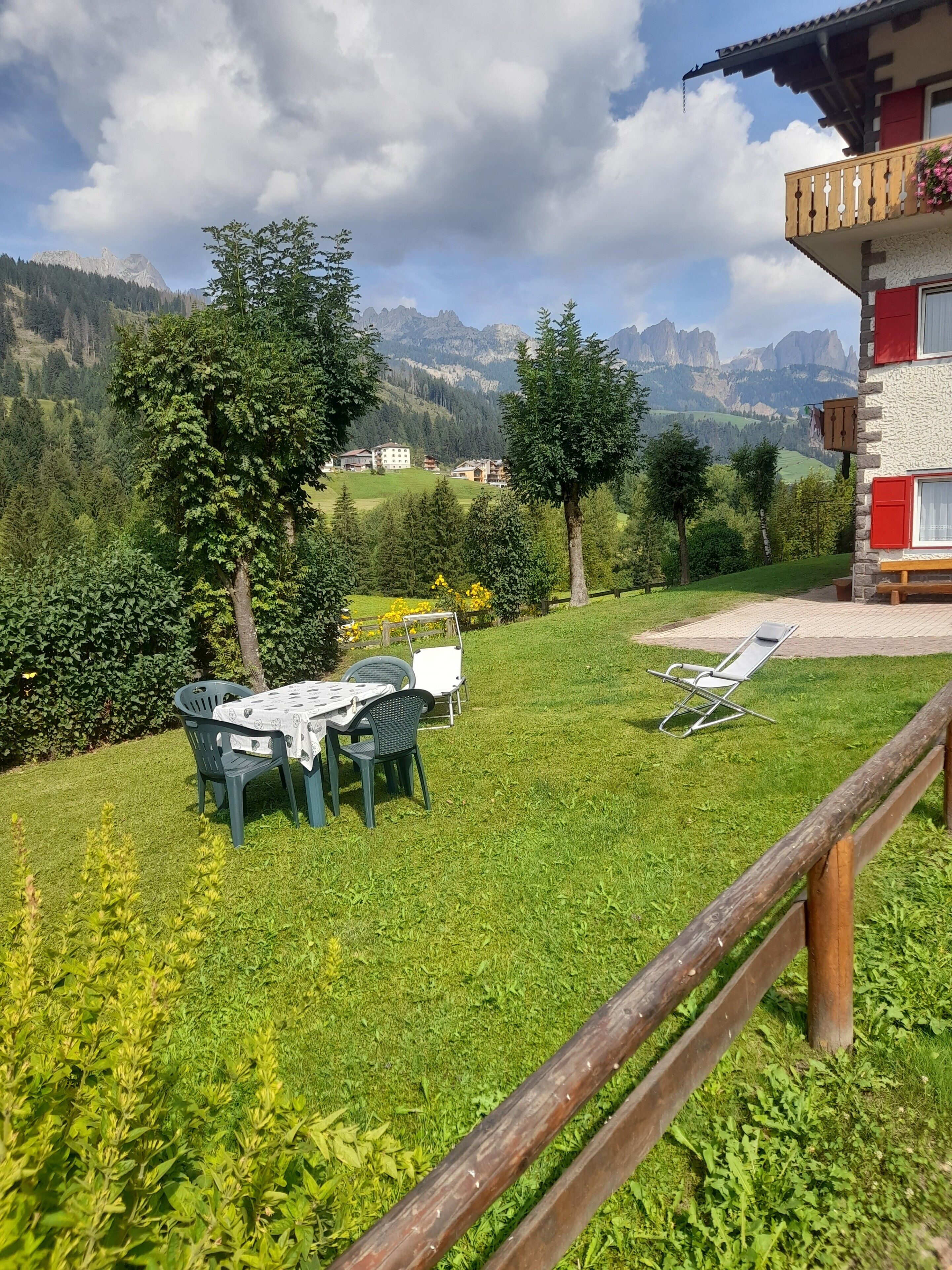 A grassy outdoor area with a table and chairs, a wooden fence, and a mountain view.