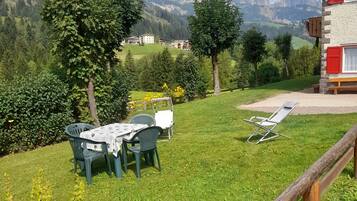 A grassy outdoor area with a table and chairs, a wooden fence, and a mountain view.
