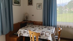 En matplats med ett bord täckt av en mönstrad duk, trästolar, en lampa och inramade tavlor på väggen.