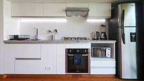 Una cocina moderna con armarios blancos, un refrigerador de acero inoxidable, un horno empotrado y un microondas.