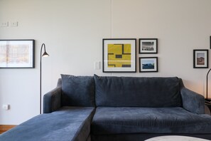 Ein modernes Wohnzimmer mit grauem Sofa, einer Stehlampe und gerahmten Kunstwerken an der Wand.