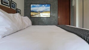 Una habitación de hotel moderna con una cama grande, un cuadro enmarcado de un paisaje y una puerta de madera.