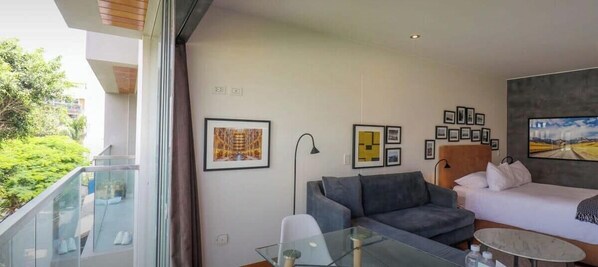 Ein modernes Hotelzimmer mit Balkon, einem Bett, einer Couch, einem Glastisch und gerahmten Kunstwerken an den Wänden.