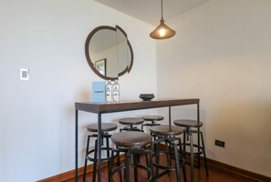 Un espace bar avec une table en bois, plusieurs tabourets, un miroir et un luminaire suspendu.