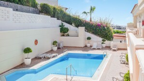 A swimming pool with steps leading down to it, surrounded by white walls and potted plants.